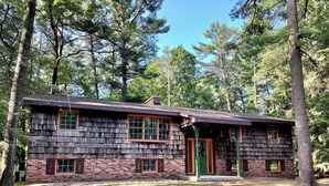 A rustic cabin with a shingled exterior, a brick foundation, and a green door.