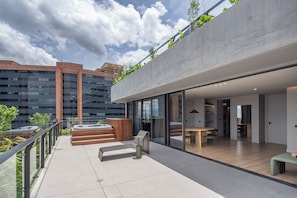 Een modern gebouw met een dakterras, inclusief een jacuzzi, zitplaatsen en een glazen balustrade met uitzicht op een stadsbeeld.