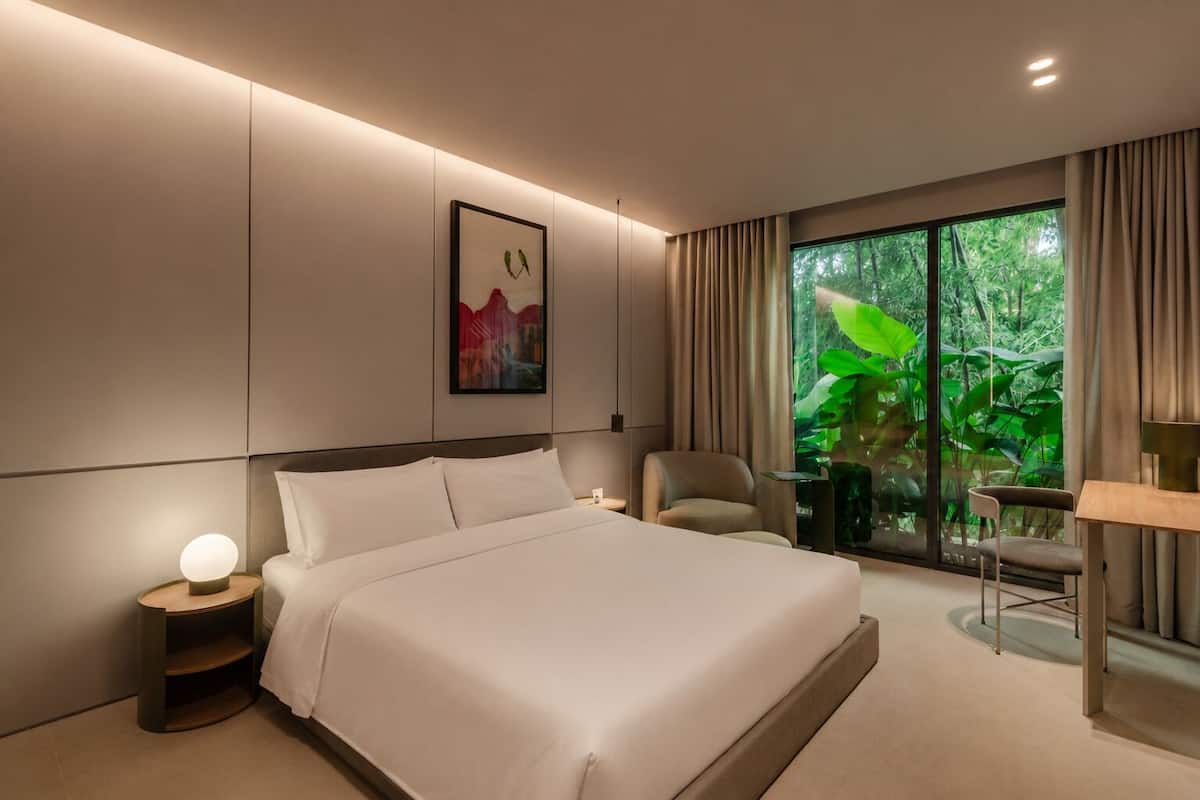 Habitación de hotel moderna con una cama grande, un escritorio, una silla y vistas a zonas verdes por la ventana.