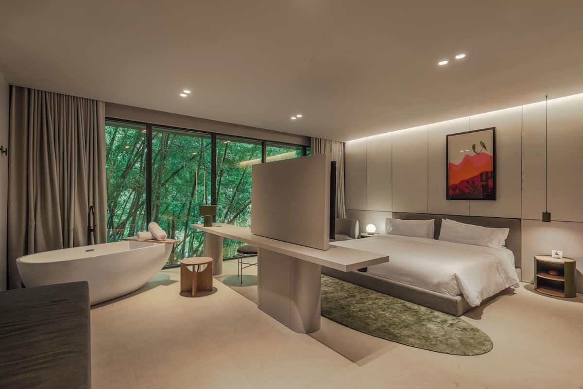 Un dormitorio moderno con un ventanal grande, una bañera, una cama y una mesita de noche.