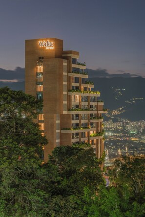 Ein mehrstöckiges Hotel mit einem auffälligen 'Wake'-Schild, Balkonen mit Bepflanzung und einer Stadtlandschaft im Hintergrund.