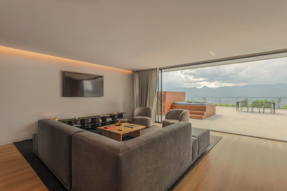 Una sala moderna con sofá, mesa de centro y televisión. Cuenta con un amplio ventanal corredera que da a un patio exterior con jacuzzi y zona de estar.