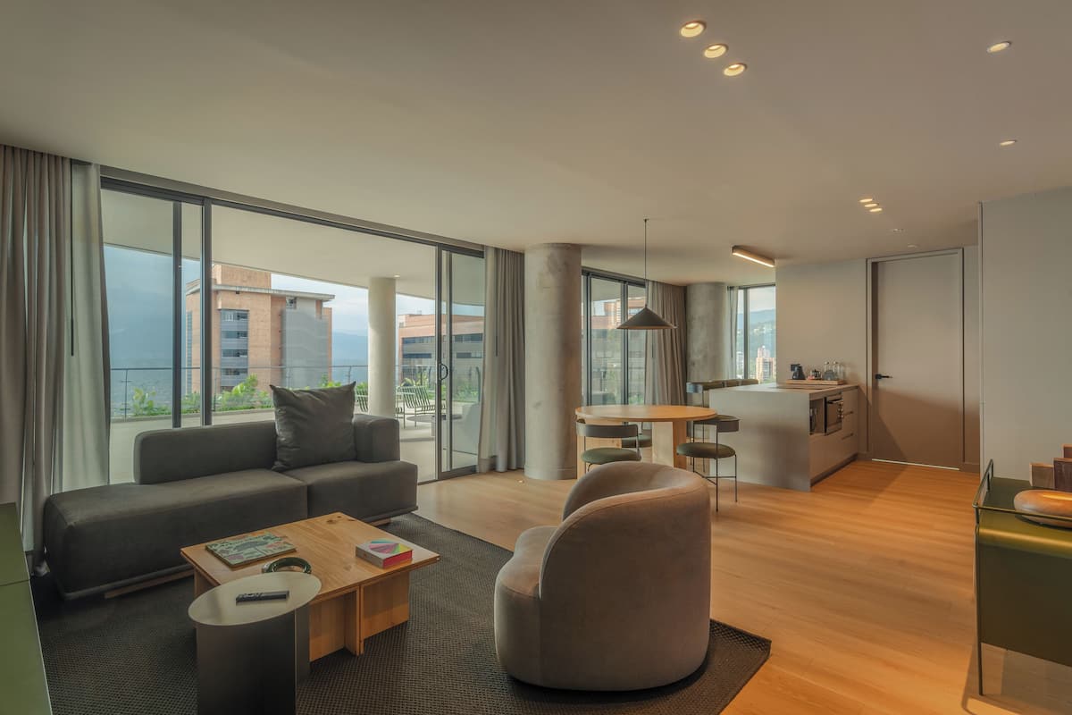 Una sala moderna con sofá, mesa de centro y sillón, un comedor con mesa y sillas, y una cocina con encimera y armarios.