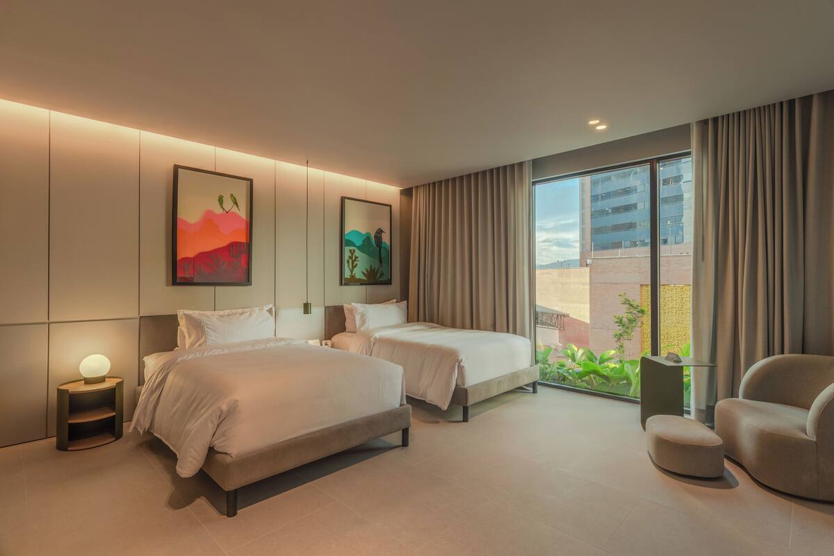 Una habitación de hotel moderna con dos camas, una zona de estar y un gran ventanal con vistas a la ciudad.