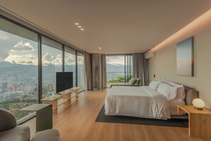 A modern hotel room with a large bed, a TV, a desk, and a view of a cityscape through large windows. - Wake BioHotel, a Member of Design Hotels (Medellín)