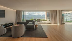 Een moderne woonkamer met een bank, fauteuils en een salontafel. Er is een groot raam met uitzicht op bergen en een balkon.