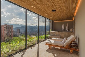 A modern rooftop lounge with large windows offering a city and mountain view, wooden ceiling, and two sun loungers. - Wake BioHotel, a Member of Design Hotels (Medellín)