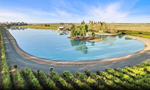 A large body of water with a curved shoreline, a small island with trees, and a building in the background. - Escape to our Lakeside Loft (Galt)
