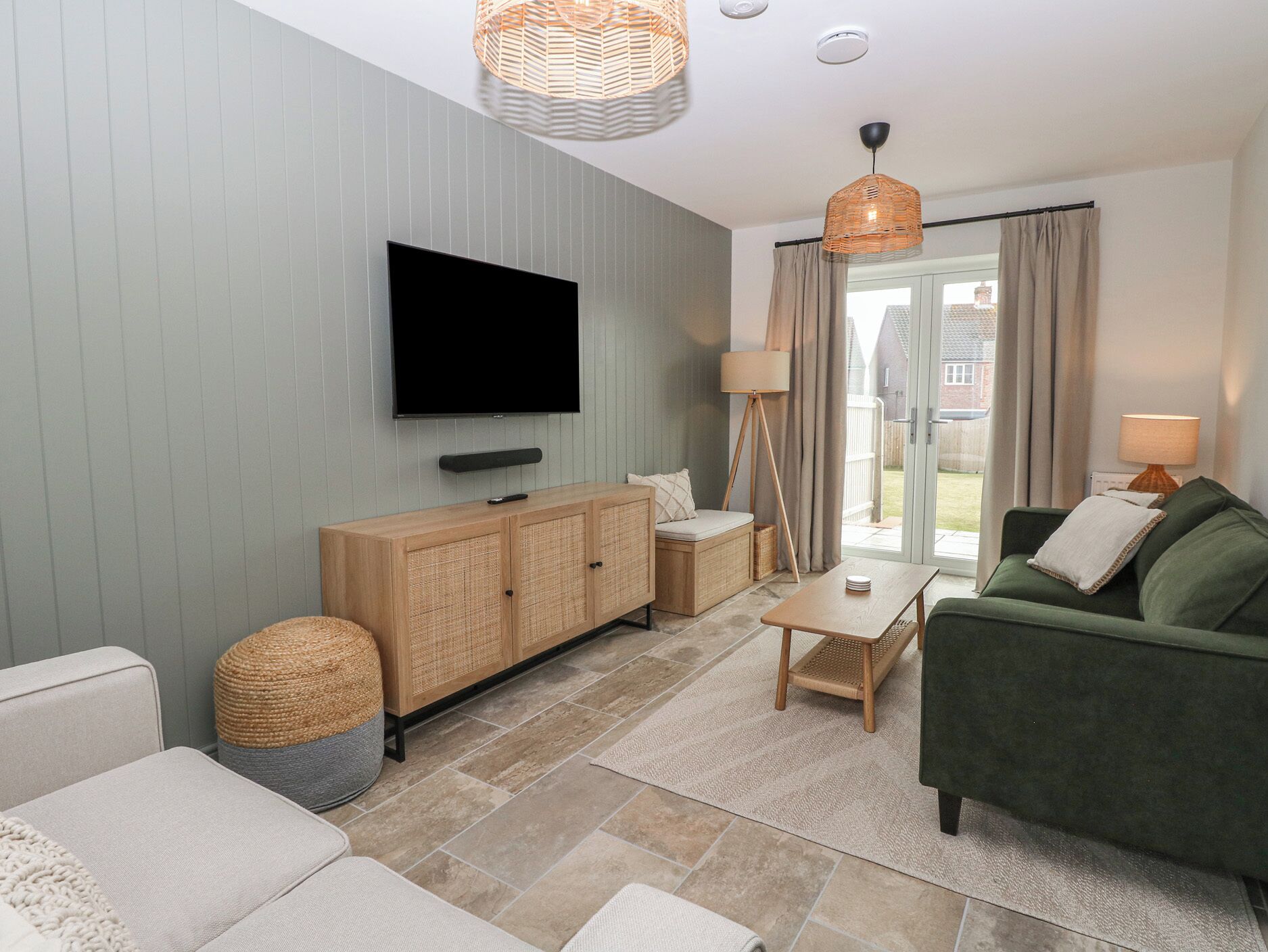 A modern living room with a flat-screen TV, a green sofa, a wooden cabinet, and a wicker floor lamp.