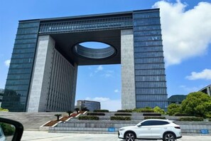 Un bâtiment moderne doté d’une grande ouverture circulaire sur sa partie supérieure, entouré d’un espace paysager avec des marches menant à cette ouverture.