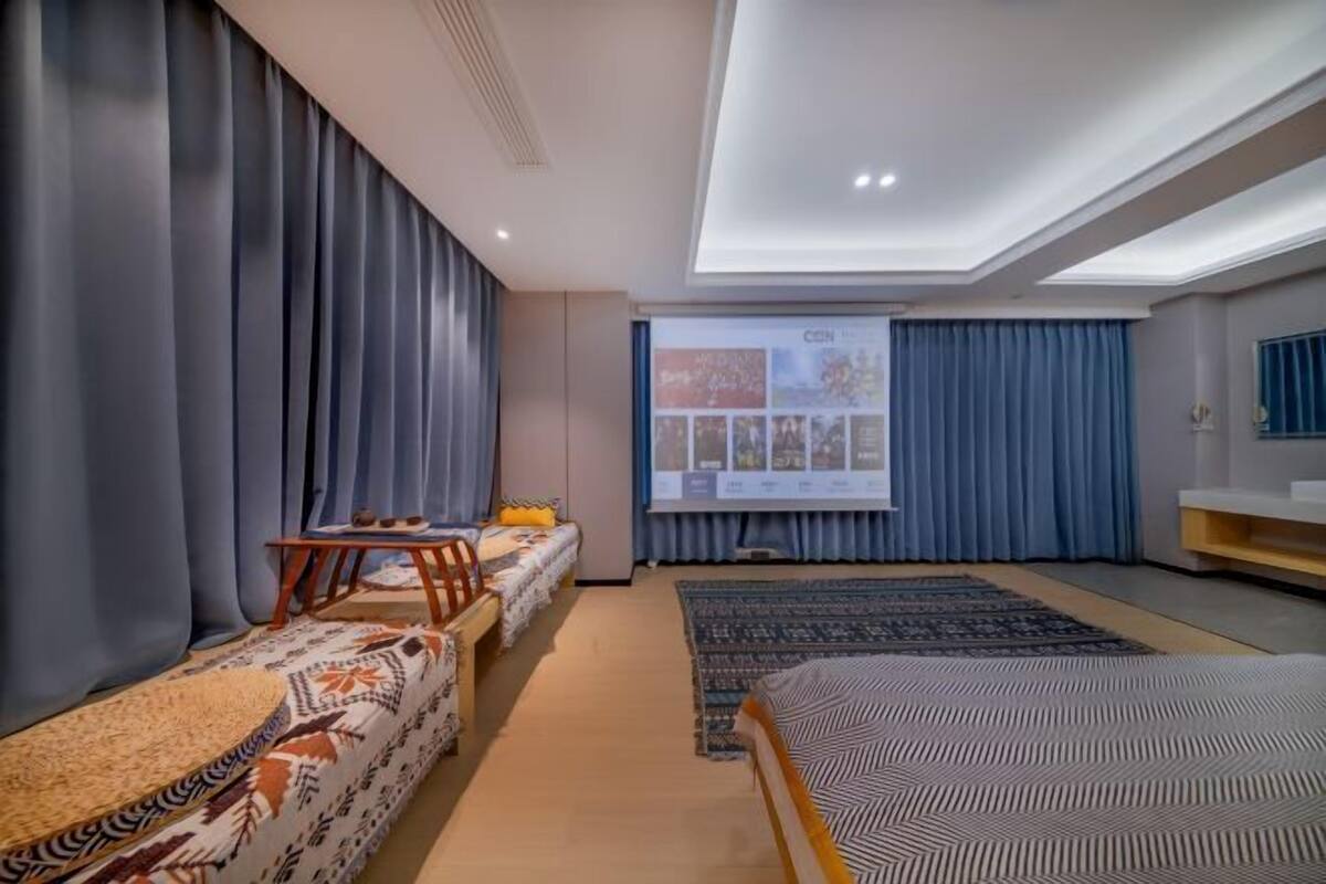 Una habitación de hotel con cama, sofá, una mesita, televisión y pantalla de proyección.