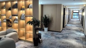 Een hotellobby met een lange gang, een zithoek met een bank, een plant en een kastenwand met kussens.