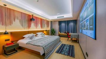 A modern hotel room with a large bed, a desk, a chair, a TV, and a ceiling light.