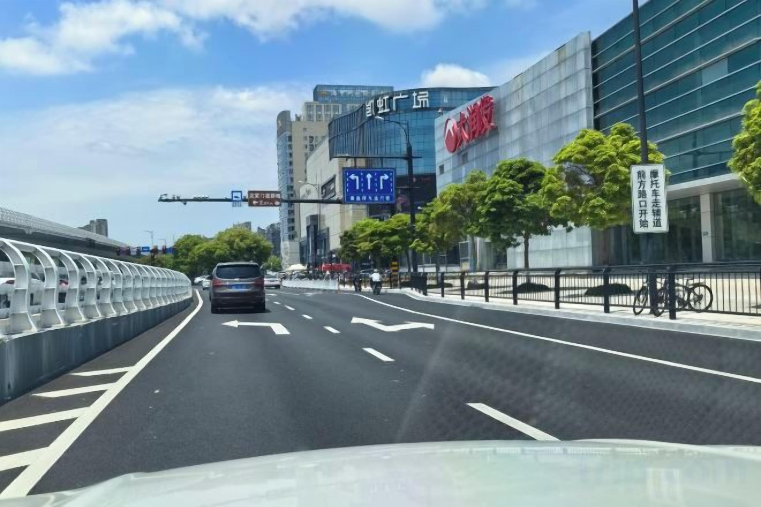 A multi-lane road with a modern building in the background, a pedestrian walkway, and a bicycle lane.