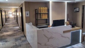 Een hotel receptie met een marmeren receptiebalie, een boekenplank met boeken en een lange gang met deuren aan weerszijden.