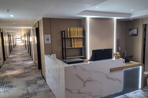 A hotel reception area with a marble reception desk, a bookshelf, and a long corridor. - Zhoushan Xingning Holiday Hotel (Zhoushan)