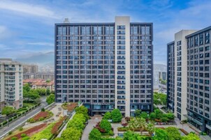 Un edificio de gran altura con un diseño arquitectónico moderno, rodeado de áreas verdes cuidadas y otros edificios residenciales.