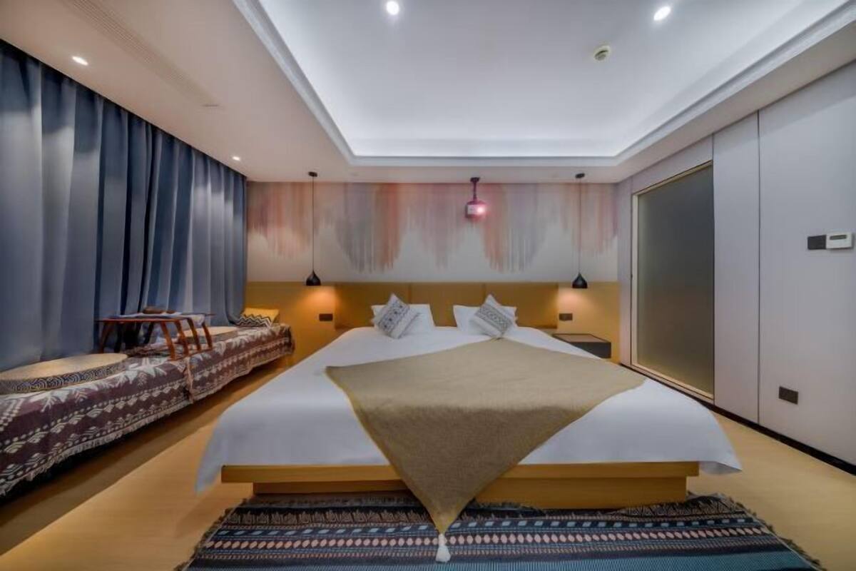 Una habitación de hotel moderna con una cama grande, mesitas de noche, un sofá y un armario amplio.