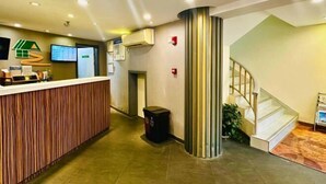 Una zona de recepción con un mostrador de madera, una pantalla digital y una escalera.
