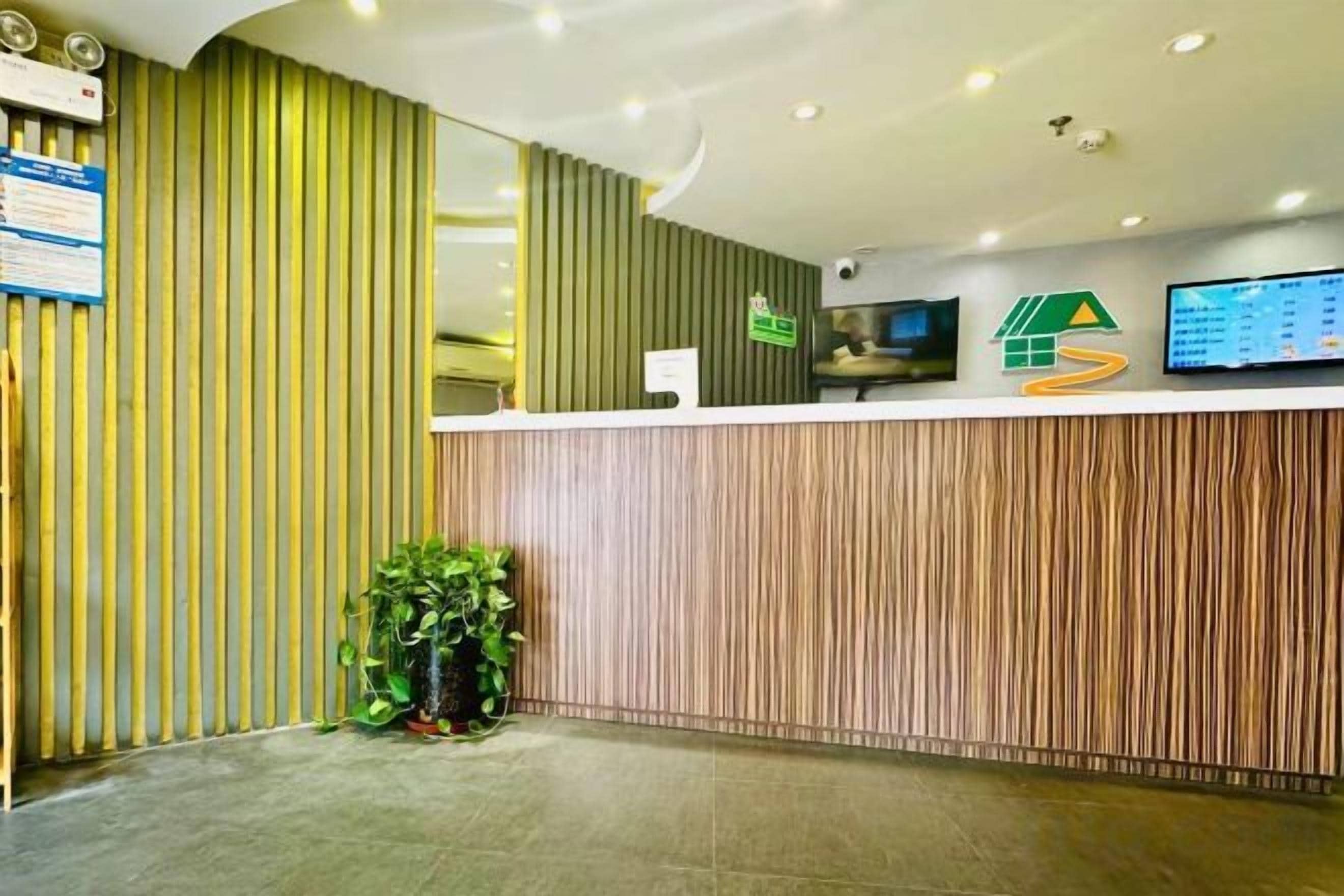 Uma área de recepção com balcão de madeira, painel vertical verde e tela digital.