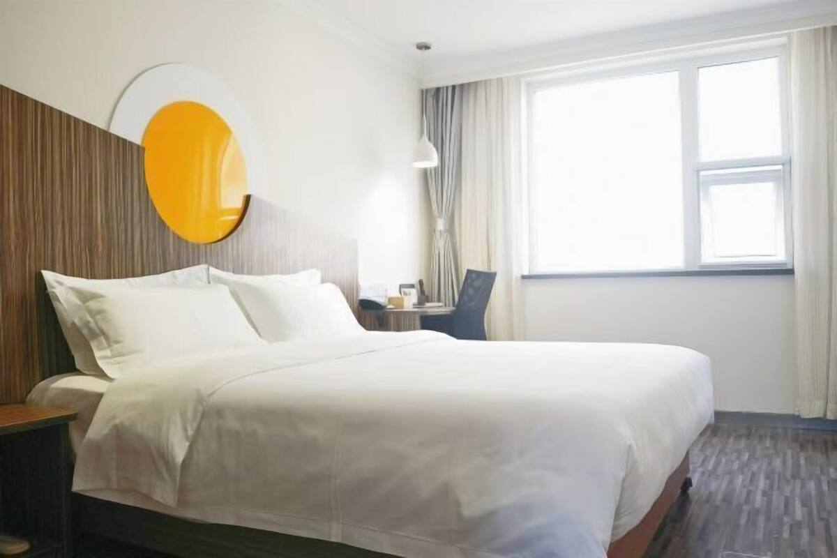 Hotelkamer met een groot bed, een bureau, een stoel, een raam met gordijnen en een spiegel aan de muur.