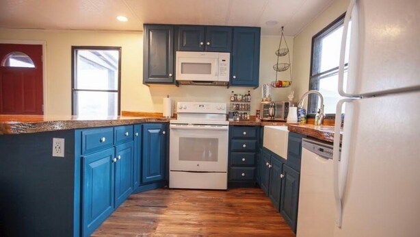 Een keuken met blauwe kastjes, een witte kookplaat en een witte koelkast.