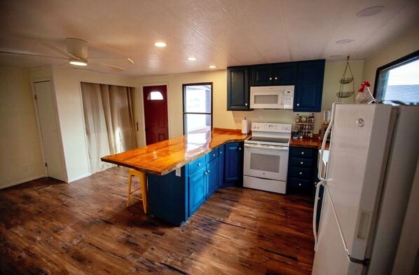 Una cocina con suelo de madera, una isla central, armarios azul oscuro y un refrigerador blanco, además de un microondas.