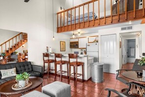 Relax in this open-plan living space with a mezzanine level, featuring a sofa, coffee table, and kitchen area with sink and refrigerator.