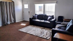 A living room with a dark-colored sofa, a patterned rug, a ceiling fan, and a door with windows. - Gila Valley Escape (Central)