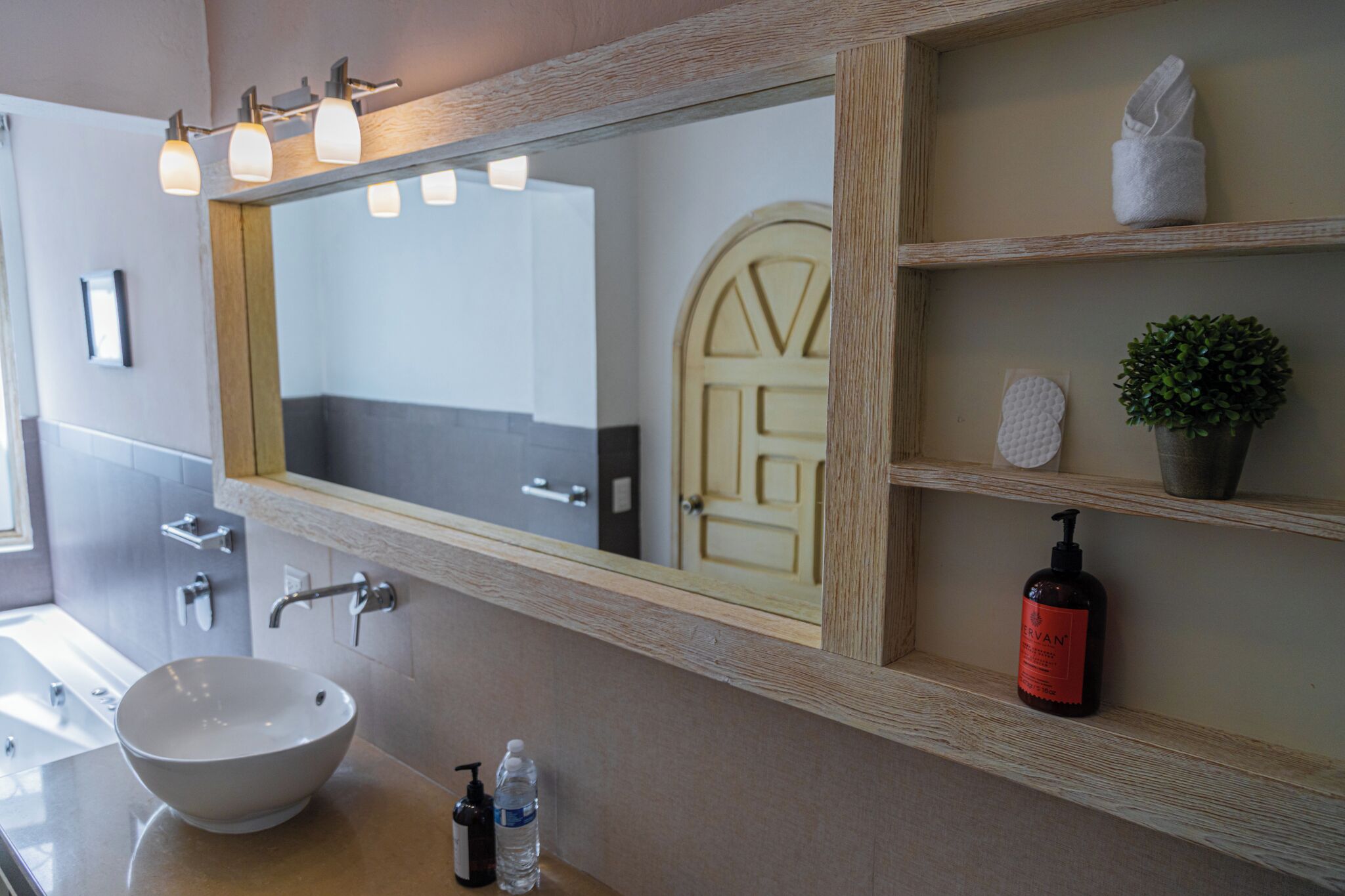 A bathroom with a large mirror, a sink with a bowl, a bottle of hand soap, a towel, and a small potted plant.