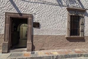 Fachada de edificio con pared texturizada, una puerta con arco y una ventana con rejas.