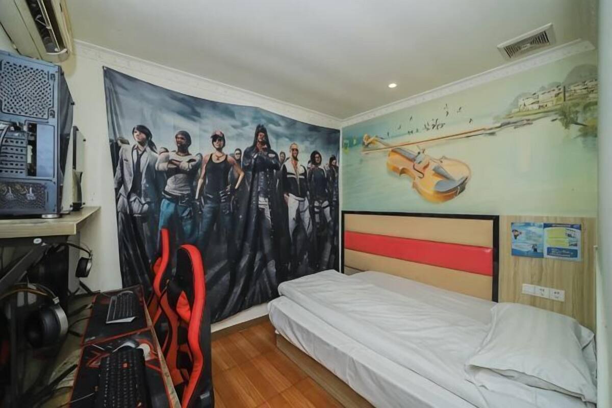 Um quarto com uma cama, uma escrivaninha com um computador, uma cadeira gamer, uma tapeçaria grande e um mural na parede.