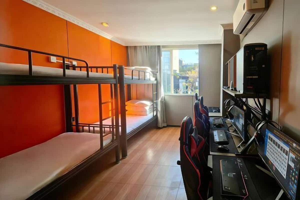 Um quarto com beliches, uma mesa com computadores e uma janela com vista para a cidade.