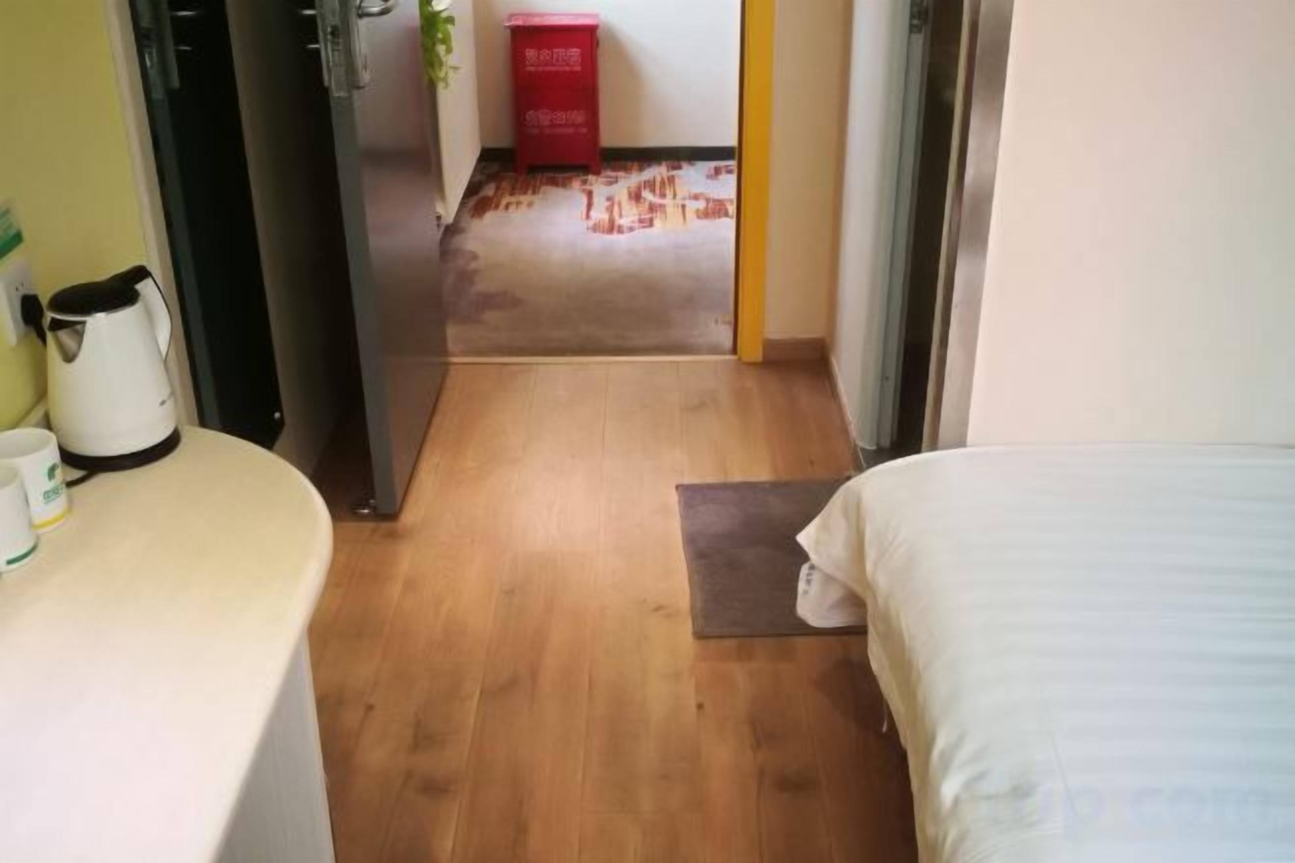 Een hotelkamer met een bed, nachtkastje, stoel en een kleintje tafeltje met een plant.