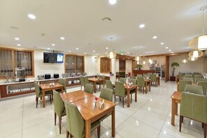 Un comedor de hotel con varias mesas y sillas, un televisor en la pared y una cocina al fondo.
