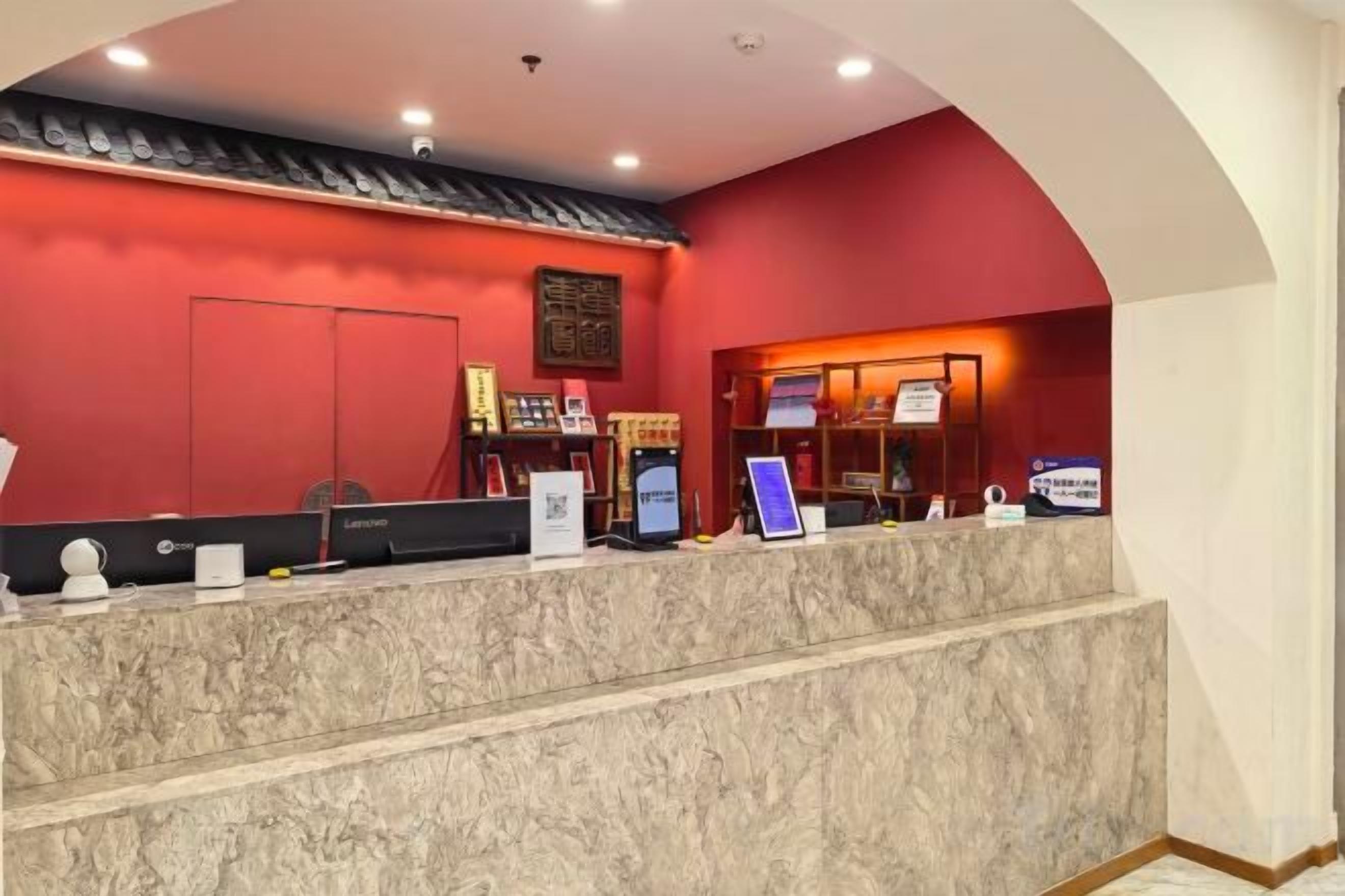A reception desk with a red wall, a computer, and a signboard.