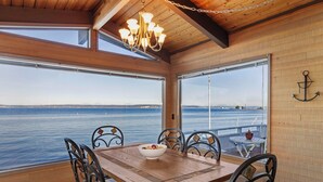 Un coin repas en bois avec vue sur la mer, un lustre et une table entourée de chaises.