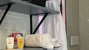 Bathroom features a shower area with a showerhead mounted on the wall and a shelf with amenities.