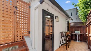 Une terrasse en bois avec des sièges d’extérieur, un barbecue et un panneau indiquant « accès interdit aux visiteurs ».