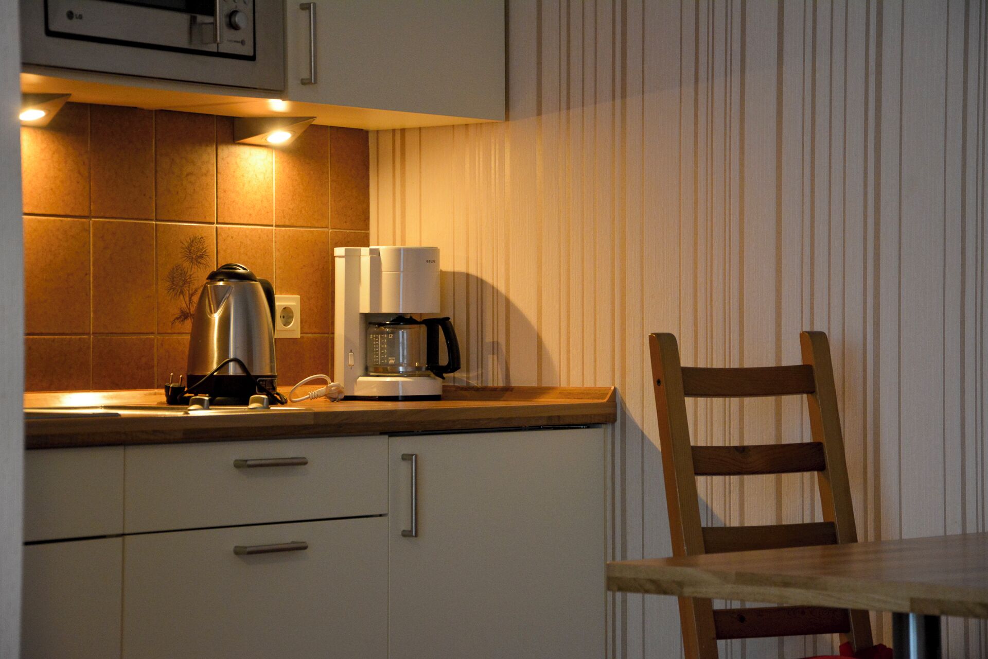 A kitchen with a coffee maker, kettle, and a wooden chair.