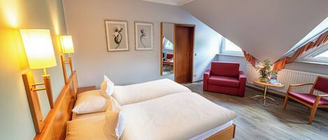Habitación de hotel con cama, dos lámparas de noche, un sillón rojo, una mesita de madera y un espejo.