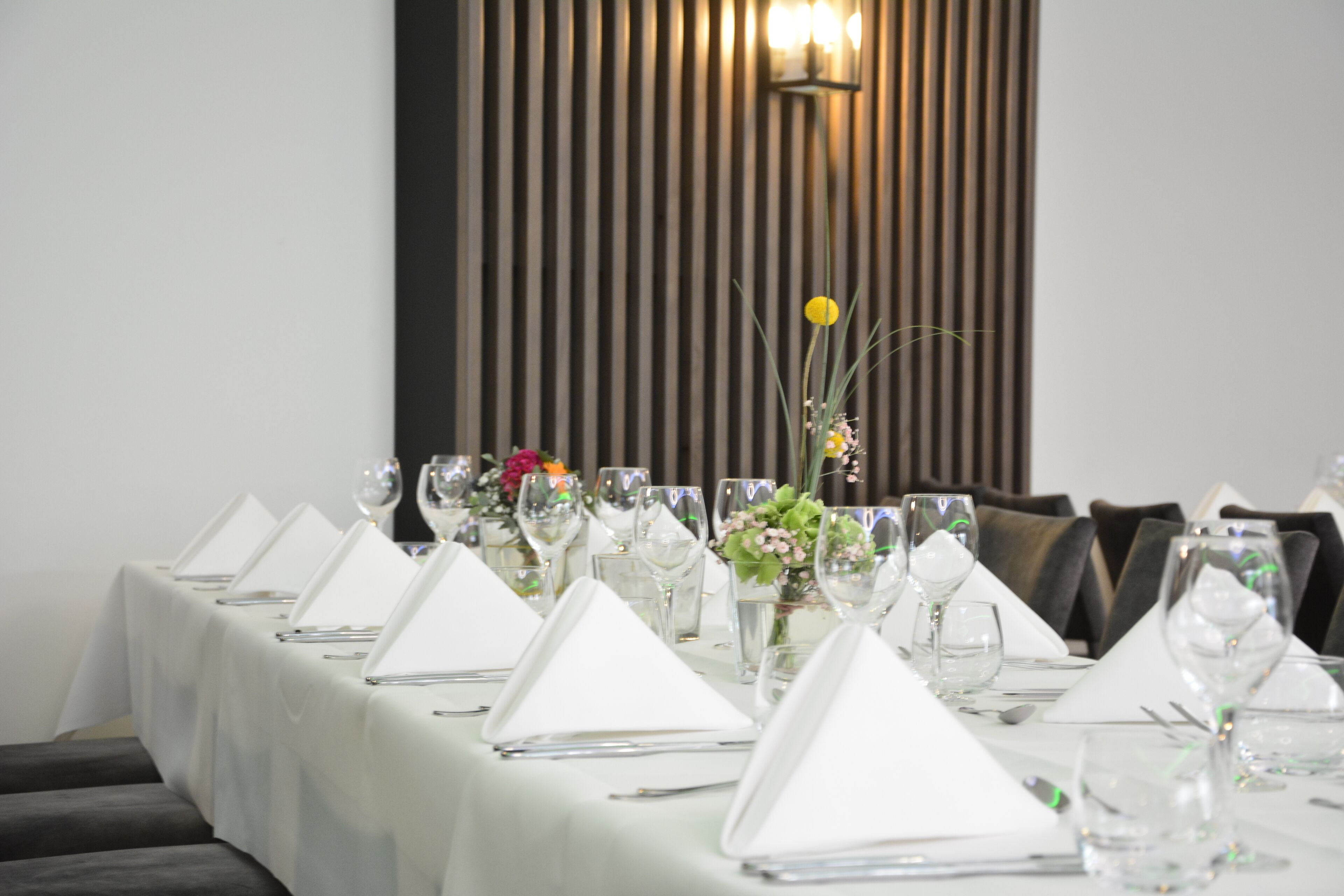 Una mesa de comedor dispuesta con manteles blancos, cristalería y centros de mesa florales.