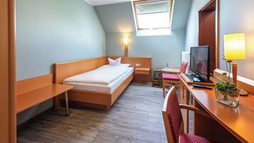 Una habitación de hotel con cama, escritorio, silla, televisor, lámpara y una pequeña mesa con una planta.