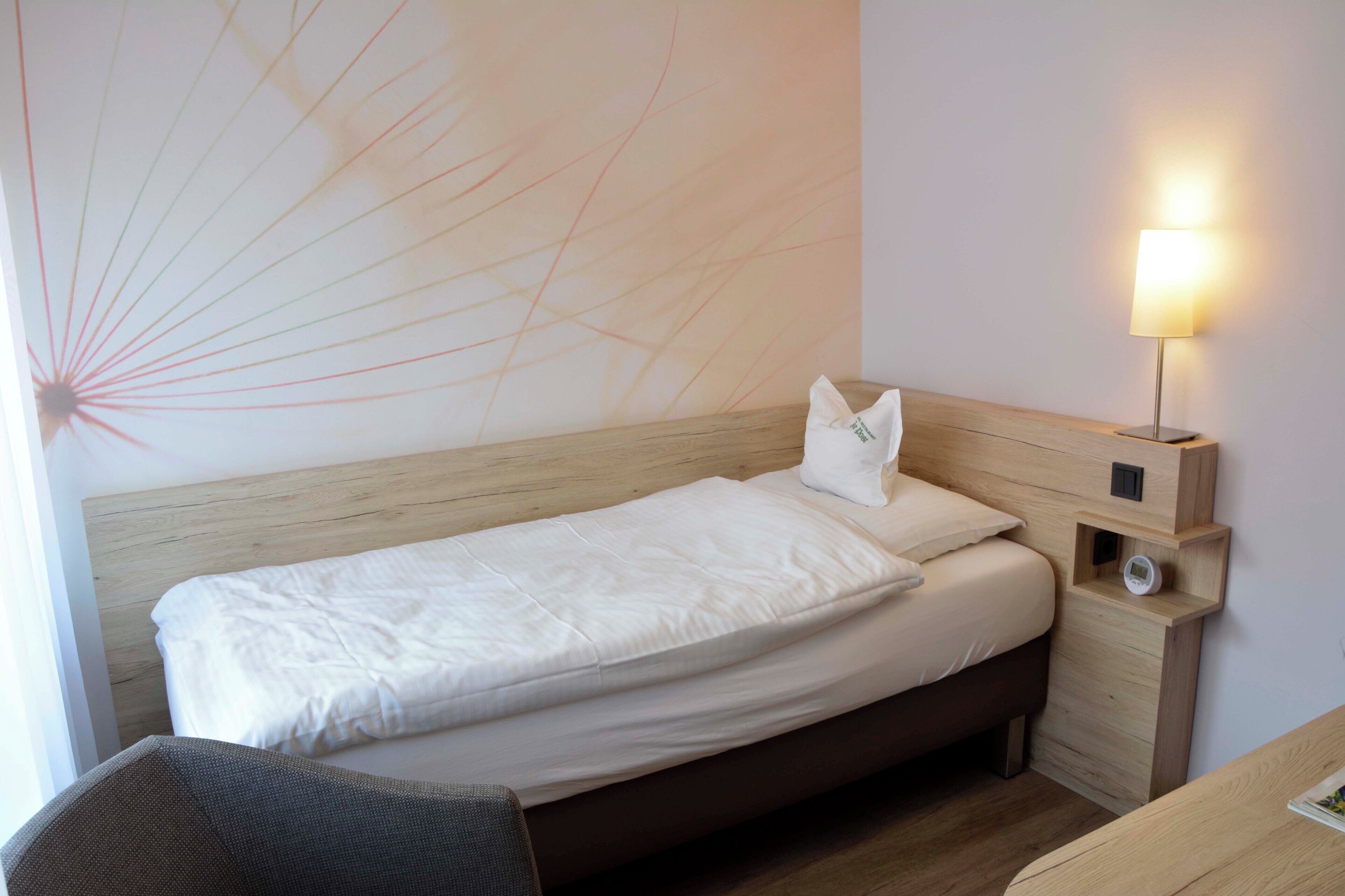 A single bed with a wooden headboard, a bedside table with a lamp, and a wall with a sunburst pattern.