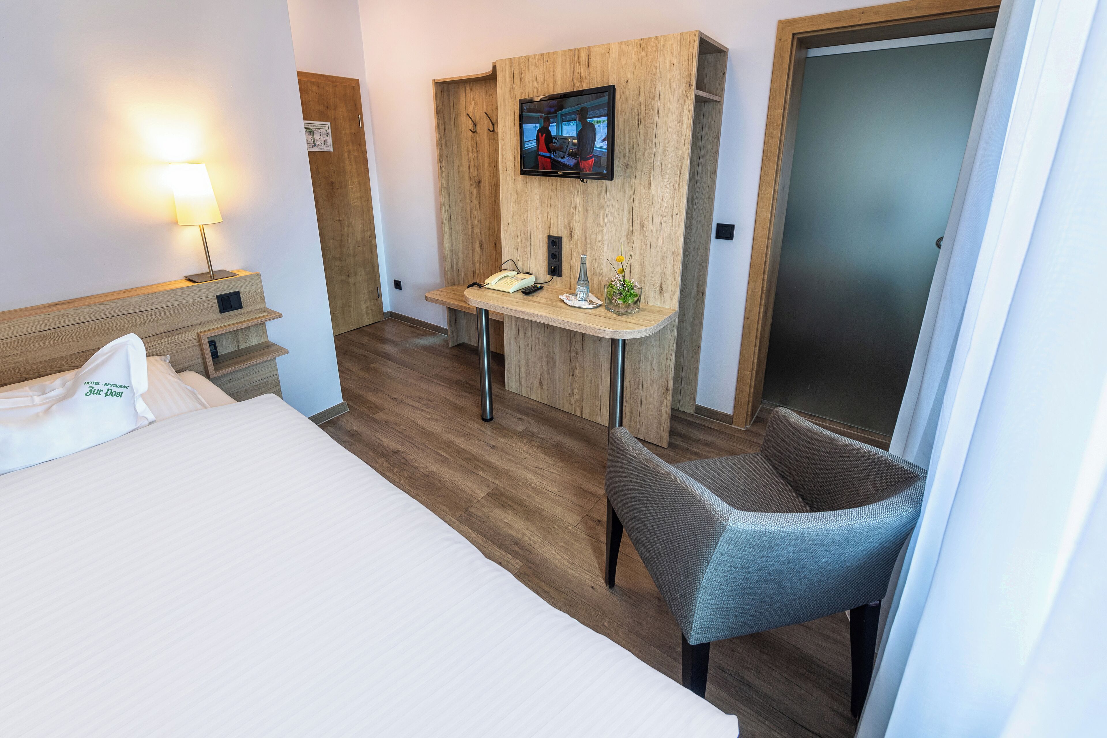 Ein Hotelzimmer mit Bett, Schreibtisch mit Stuhl, Fernseher und Lampe.