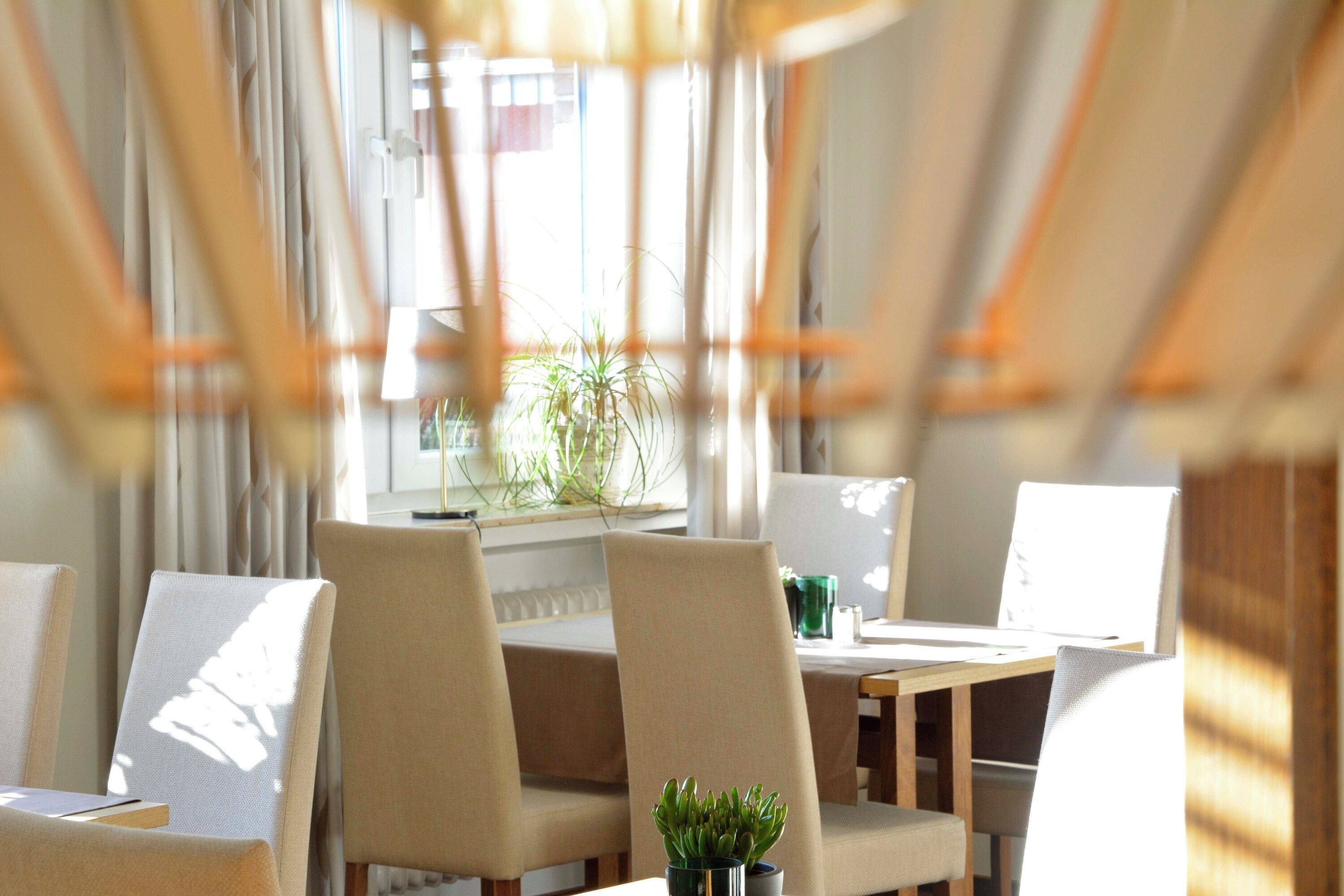 Un comedor con una mesa, sillas, una planta en maceta y un ventanal con cortinas.