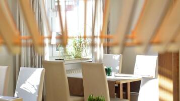 Un comedor con una mesa, sillas, una planta en maceta y un ventanal con cortinas.