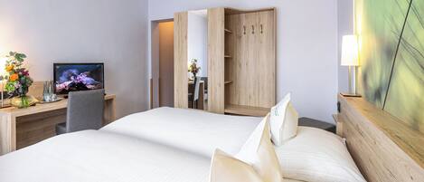 Habitación de hotel con dos camas, un escritorio con computadora, televisor y un armario de madera.