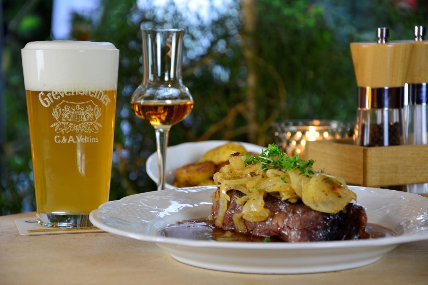 A glass of beer, a bottle, and a plate of food on a table.