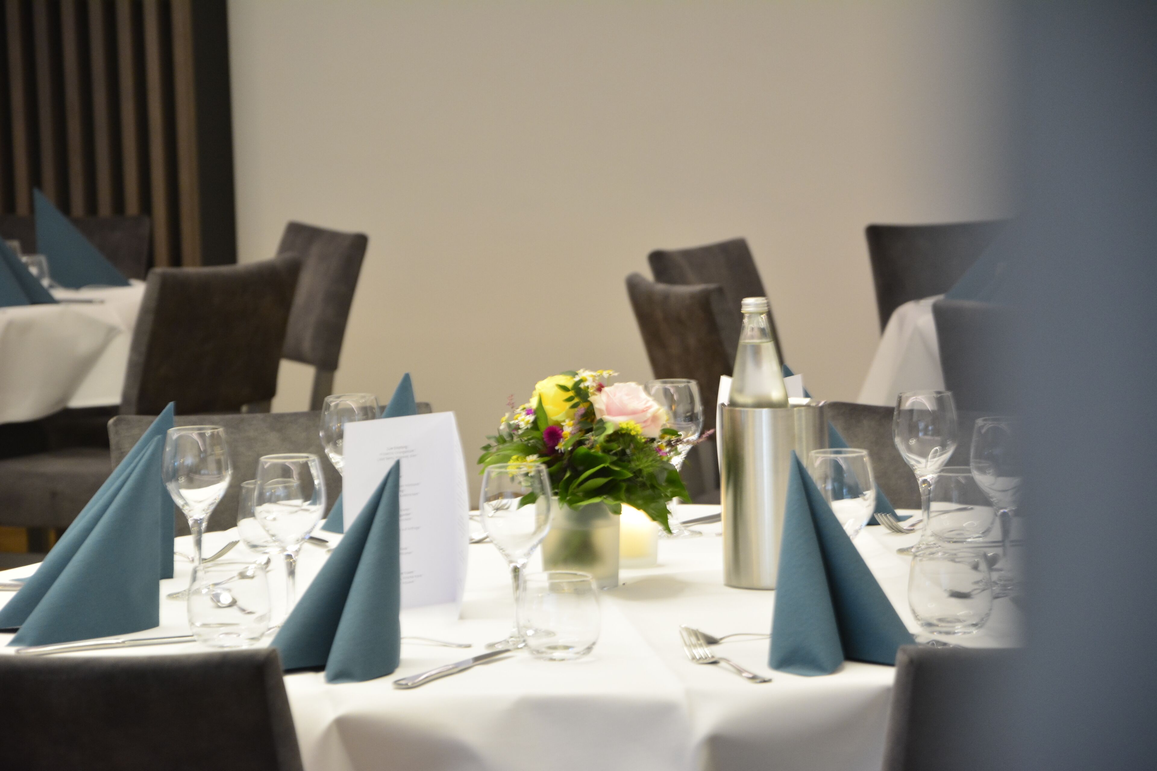 A dining table set with blue napkins, wine glasses, and a centerpiece of flowers.